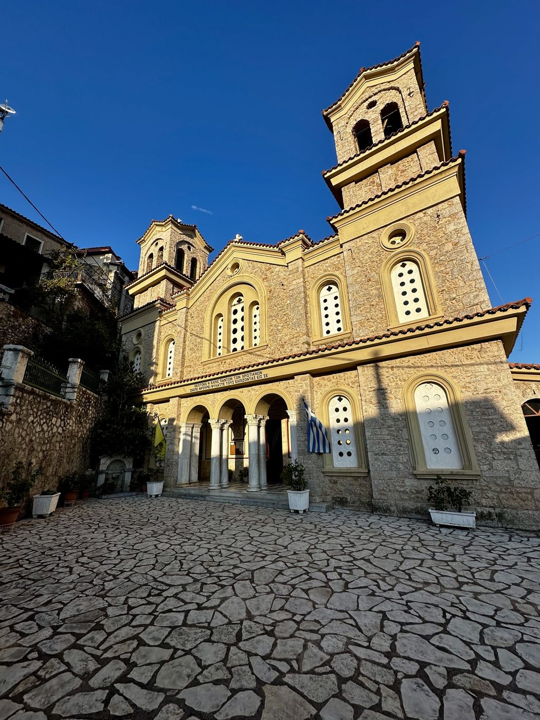 A stone church with two bell towers and a cobblestone square in Arachova