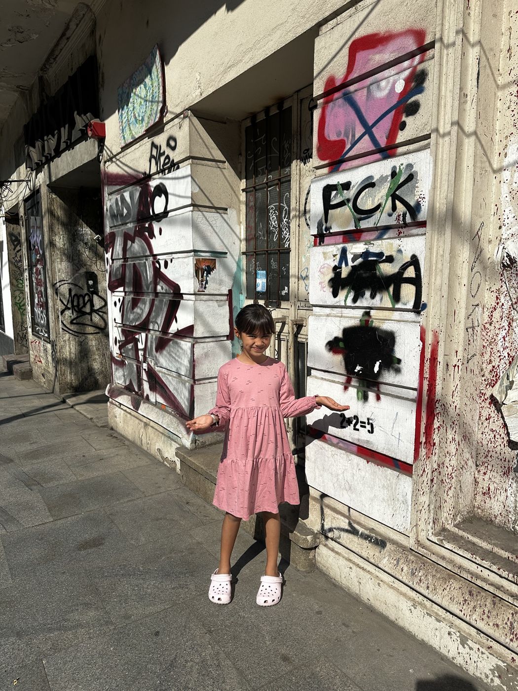 Olivia shrugging in front of a graffiti-covered building in our neighborhood