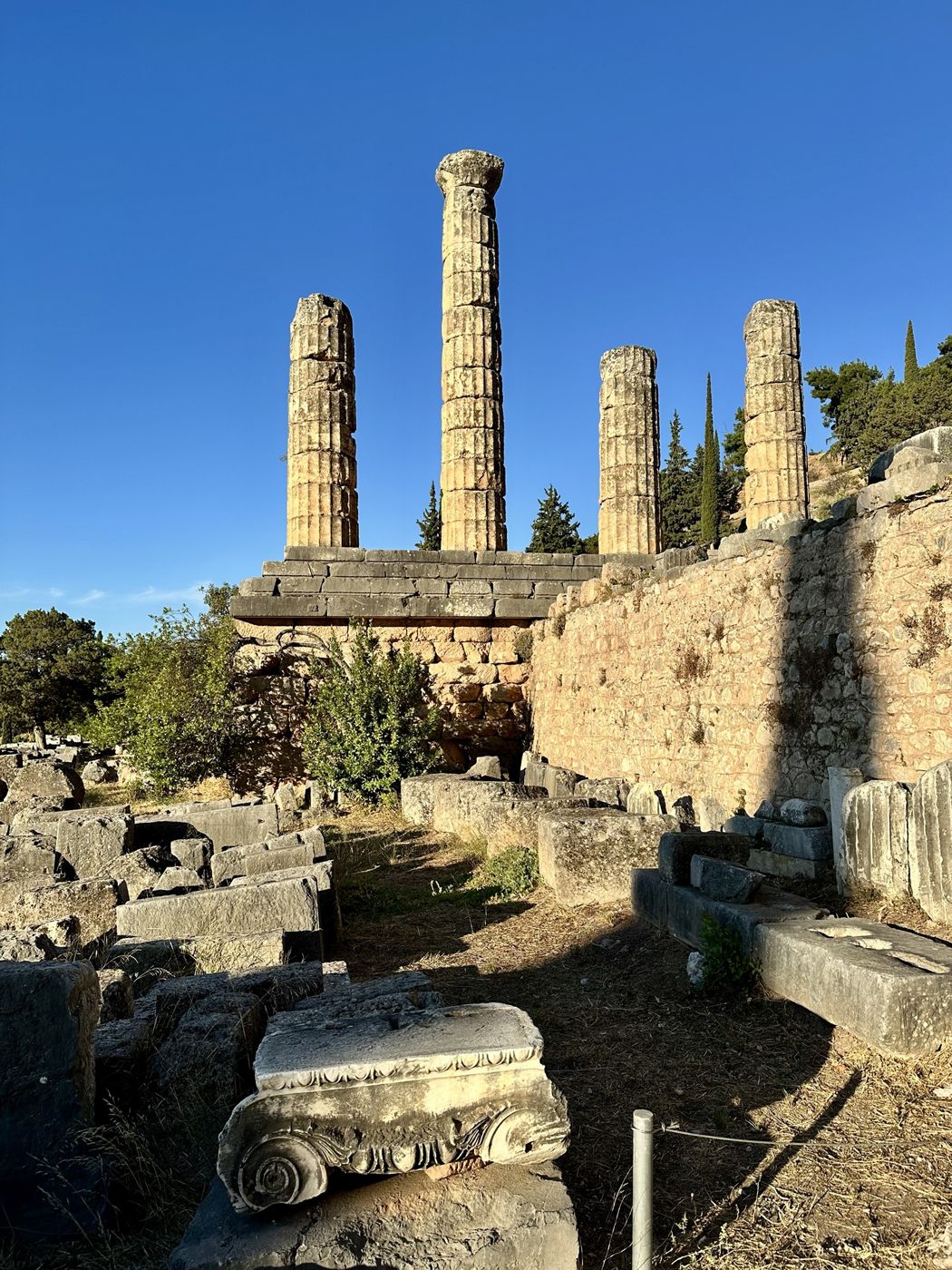 The four standing columns of the Temple of Apollo at Delphi, with a carved stone capital in the foreground