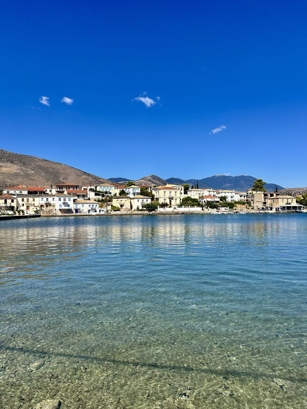 The clear turquoise harbor of Galaxidi with pastel houses and mountains behind